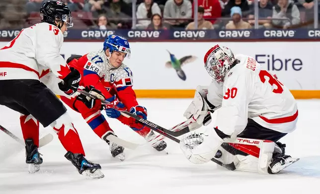 Canada goaltender Carter George makes a save on Czechia's Petr Sikora while Canada's Ethan MacKenzie, right, defends, during the first period of an IIHF World Junior Hockey Championship game in Minneapolis, Friday, Dec. 26, 2025. (Christopher Katsarov/The Canadian Press via AP)