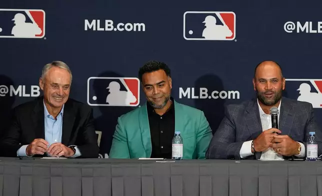 Rob Manfred, left, commissioner of Major League Baseball, Nelson Cruz, center, former baseball player and general manager of the Dominican National team, and Albert Pujols, former baseball player and manager of a Dominican professional baseball team, take part in a news conference at the MLB winter meetings, Monday, Dec. 8, 2025, in Orlando, Fla. (AP Photo/John Raoux)