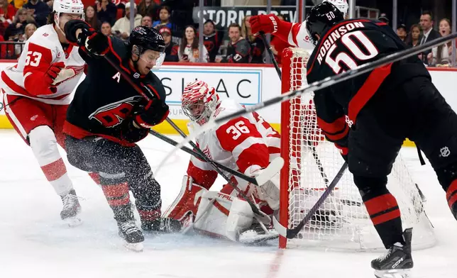 Carolina Hurricanes' Eric Robinson (50) stuffs the puck past Detroit Red Wings goaltender John Gibson (36) for a goal with teammate Sebastian Aho and Red Wings' Moritz Seider (53) nearby during the second period of an NHL hockey game in Raleigh, N.C., Saturday, Dec. 27, 2025. (AP Photo/Karl DeBlaker)