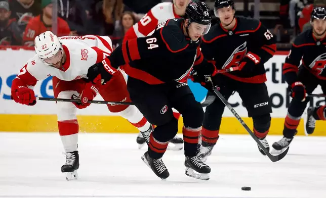 Carolina Hurricanes' Joel Nystrom (64) tries to control the puck with Detroit Red Wings' Michael Rasmussen (27) nearby during the first period of an NHL hockey game in Raleigh, N.C., Saturday, Dec. 27, 2025. (AP Photo/Karl DeBlaker)