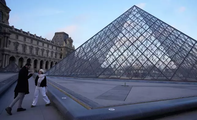 People stand by the pyramid of the Louvre museum as workers at the Louvre will vote to go on strike or continue talks with the government after months of mounting pressure on the world's most visited museum, Monday, Dec. 15, 2025 in Paris. (AP Photo/Michel Euler)