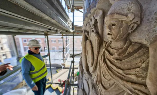 A journalist looks at bas-reliefs on the second-century A.D. Column of Marcus Aurelius in central Rome during a media tour, Thursday, Dec. 18, 2025. (AP Photo/Domenico Stinellis)