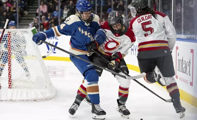 Vancouver Goldeneyes' Hannah Miller (34) hits Ottawa Charge's Brooke Hobson (11) as Rory Guilday (5) watches during the third period of a PWHL hockey game in Vancouver, British Columbia, Tuesday, Dec. 16, 2025. (Ethan Cairns/The Canadian Press via AP)