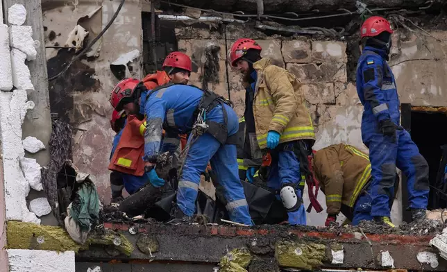 Rescuers put fragments of a body of the victim into a plastic bag after Russian drone hit a multi-storey apartment building during massive missile and drone attack in Kyiv, Ukraine, Saturday, Dec. 27, 2025. (AP Photo/Efrem Lukatsky)