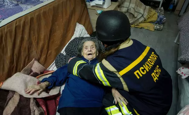 A psychologist of a rescue team helps en elderly woman at the hospice which was damaged after a Russian strike on Kyiv, Ukraine, on Saturday, Dec. 27, 2025. (AP Photo/Evgeniy Maloletka)