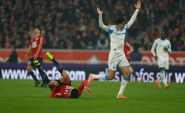 Lille's Olivier Giroud, bottom, lies on the pitch as Marseille's Nayef Aguerd reacts during the French League One soccer match between Lille and Marseille in Villeneuve-d'Ascq, outside Lille, France, Friday, Dec. 5, 2025. (AP Photo/Jean-Francois Badias)