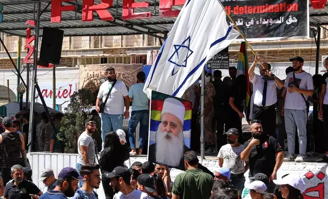 FILE - A man waves an Israeli flag over a picture of Sheikh Mowafak Tarif, the spiritual leader of the Druze in Israel, during a weekly rally in Sweida, southern Syria, on Sept. 20, 2025. (AP Photo/Fahd Kiwan, File)