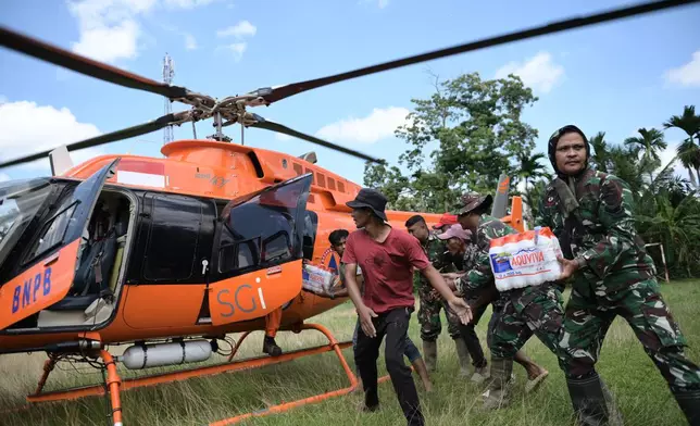 Soldiers and residents unload relief goods from a national disaster mitigation agency's helicopter during an aerial aid distribution in a flood affected area in North Aceh, Indonesia, Thursday, Dec. 4, 2025. (AP Photo/Reza Saifullah)