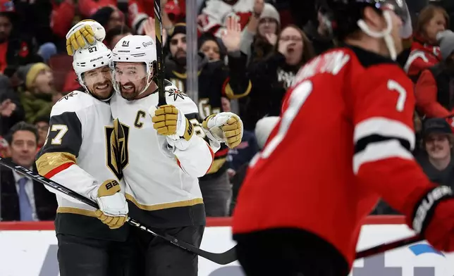 Vegas Golden Knights defenseman Shea Theodore (27) is congratulated after scoring a goal by Mark Stone (61) during the first period of an NHL hockey game against the New Jersey Devils, Friday, Dec. 5, 2025, in Newark, N.J. (AP Photo/Adam Hunger)