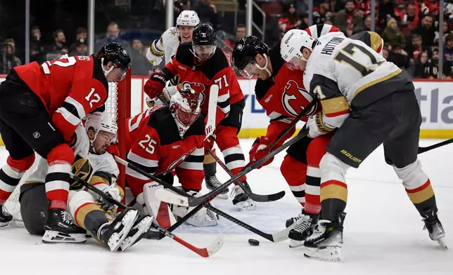 New Jersey Devils goaltender Jacob Markstrom (25) defends his net against Vegas Golden Knights center Tomas Hertl, on ice, and defenseman Ben Hutton (17) during the first period of an NHL hockey game Friday, Dec. 5, 2025, in Newark, N.J. (AP Photo/Adam Hunger)