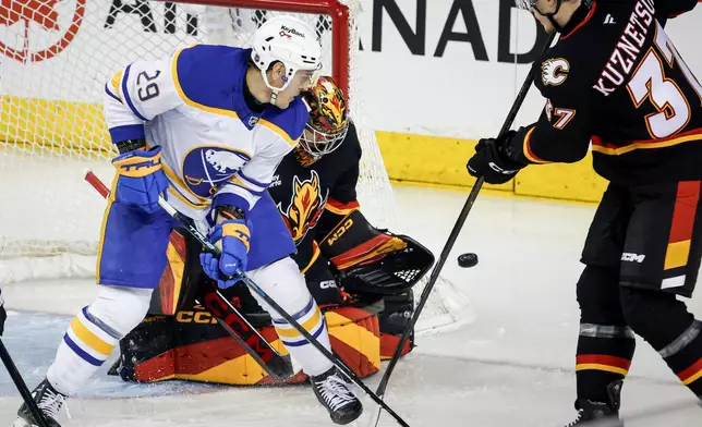 Buffalo Sabres' Beck Malenstyn, left, looks on as Calgary Flames goalie Dustin Wolf deflects a shot while Yan Kuznetsov defends during the first period of an NHL hockey game in Calgary, Alberta, Monday, Dec. 8, 2025. (Jeff McIntosh/The Canadian Press via AP)