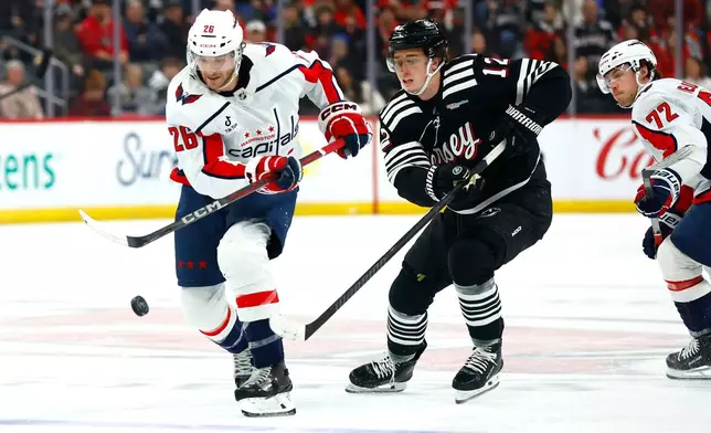 Washington Capitals center Nic Dowd (26) plays the puck against New Jersey Devils center Cody Glass, center, during the first period of an NHL hockey game, Saturday, Dec. 27, 2025, in Newark, N.J. (AP Photo/Noah K. Murray)