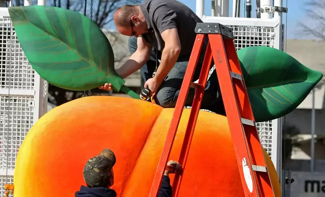 FILE - Gary Seputis, top, and Clint Hornsby, employees of Entertainment Design Group, work on attaching two leaves to the fiberglass and foam Peach in preparation for the 2012 Peach Drop at Underground Atlanta, Friday, Dec. 30, 2011, in Atlanta. ( Jason Getz/Atlanta Journal-Constitution via AP, File)