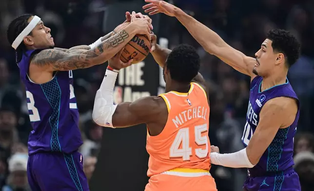 Charlotte Hornets guard Tre Mann, left, and guard Josh Green, right, defend against Cleveland Cavaliers guard Donovan Mitchell in the first half of an NBA basketball game, Monday, Dec. 22, 2025, in Cleveland. (AP Photo/David Dermer)