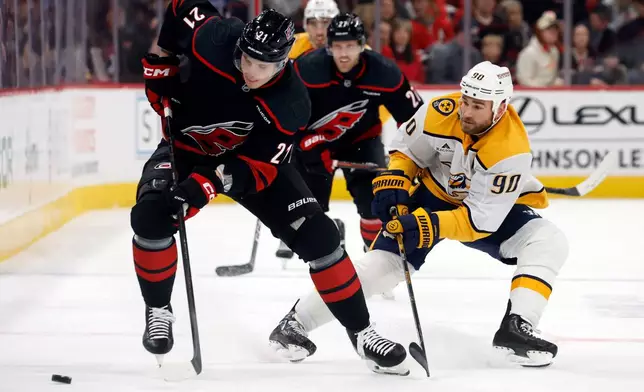 Carolina Hurricanes' Alexander Nikishin (21) battles for the puck with Nashville Predators' Ryan O'Reilly (90) during the first period of an NHL hockey game in Raleigh, N.C., Saturday, Dec. 6, 2025. (AP Photo/Karl DeBlaker)