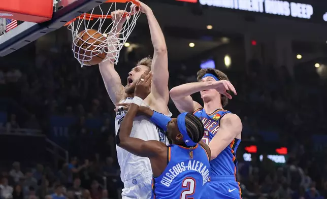 Memphis Grizzlies center Jock Landale, left, dunks next to Oklahoma City Thunder guard Shai Gilgeous-Alexander (2) and center Branden Carlson, top right, during the first half of an NBA basketball game Monday, Dec. 22, 2025, in Oklahoma City. (AP Photo/Nate Billings)