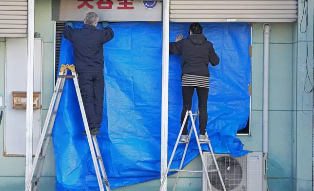 People cover the broken glasses with a blue sheet at a beauty salon in Hachinohe, Aomori prefecture, northern Japan Tuesday, Dec. 9, 2025, following a powerful earthquake on late Monday. (Kazuki Kozaki/Kyodo News via AP)
