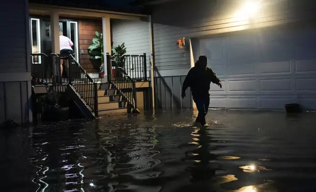 Haji Higa, right, and Lydia Heglin, left, walk through floodwaters at their front door after heavy rains led to historic flooding in the region Saturday, Dec. 13, 2025, in Burlington, Wash. (AP Photo/Lindsey Wasson)