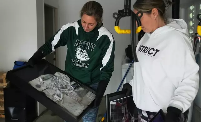 Mandy McColl, right, looks over as friend Marielle Hinderman shows a jersey signed by kids coached by her husband, Todd, after it was caught in floodwaters that reached their home in the region Saturday, Dec. 13, 2025, in Burlington, Wash. (AP Photo/Lindsey Wasson)