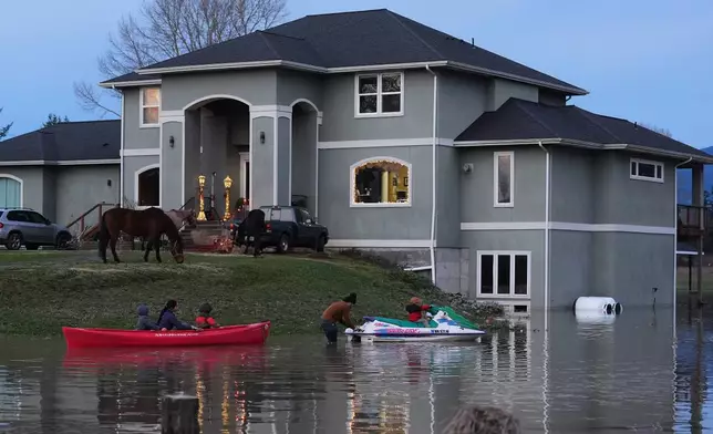 "E-man" Trujillo, center, uses a jet-ski to tow a canoe with his children Liam, 6, far left, Julissa, 15, and Benjamin, 5, third from left, as their horses take refuge on the high ground at their front door after heavy rains led to historic flooding in the region Saturday, Dec. 13, 2025, in Burlington, Wash. (AP Photo/Lindsey Wasson)