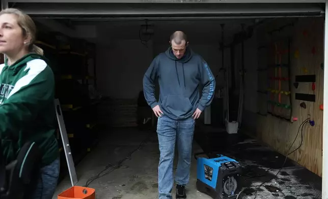 Todd Hinderman, right, and wife Marielle Hinderman, left, walk out of their garage after the lower level of their home flooded after heavy rains in the region Saturday, Dec. 13, 2025, in Burlington, Wash. (AP Photo/Lindsey Wasson)