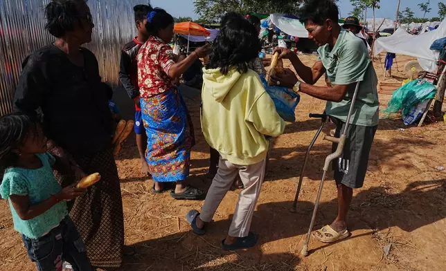 A disabled man, right, receives bread from a local charity group as he takes refuge in Wat Prasat Srahkandal, Banteay Menchey province, Cambodia, Sunday, Dec. 14, 2025, after fleeing home following fighting between Thailand and Cambodia over territorial claims. (AP Photo/Heng Sinith)