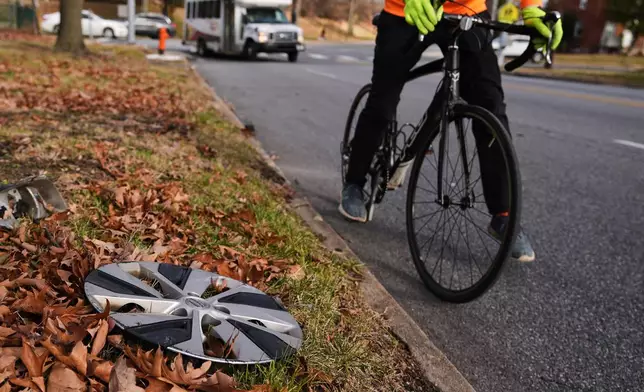 Cyclist Barnaby Wickham steps down and dismounts his bike after spotting a lost hubcap on the side of the road, Thursday, Dec. 11, 2025, in Baltimore. (AP Photo/Stephanie Scarbrough)