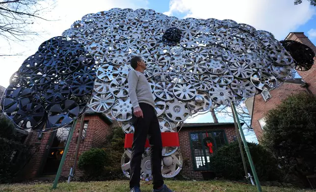 Cyclist Barnaby Wickham poses for a portrait in front of his art structure made from hubcaps, Thursday, Dec. 11, 2025, at his home in Baltimore. (AP Photo/Stephanie Scarbrough)