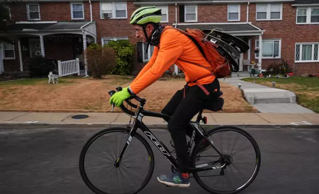 With hubcaps fastened to his backpack, cyclist Barnaby Wickham pedals through a neighborhood on his journey home, Thursday, Dec. 11, 2025, in Baltimore. (AP Photo/Stephanie Scarbrough)