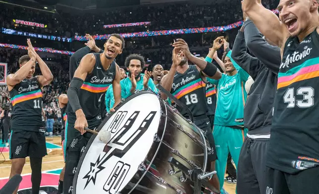 San Antonio Spurs forward Victor Wembanyama (1) hits on a drum as he and teammates celebrate with the Spurs fans after defeating the Oklahoma Thunder in an NBA basketball game in San Antonio, Tuesday, Dec. 23, 2025. (AP Photo/Rodolfo Gonzalez)