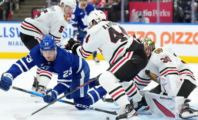 Toronto Maple Leafs forward Matthew Knies (23) gets knocked down by Chicago Blackhawks defenceman Wyatt Kaiser (44) as teammate Spencer Knight (30) makes the save during second period NHL hockey action in Toronto, Tuesday, Dec. 16, 2025. (Nathan Denette/The Canadian Press via AP)
