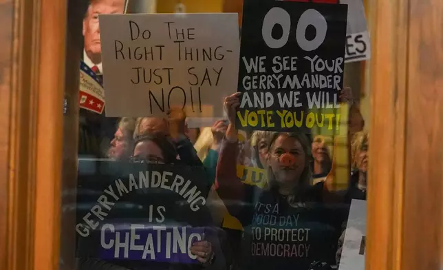 Protesters are seen through a window in the Senate Chamber during dissuasion before a vote to redistrict the state's congressional map, Thursday, Dec. 11, 2025, at the Statehouse in Indianapolis. (AP Photo/Michael Conroy)