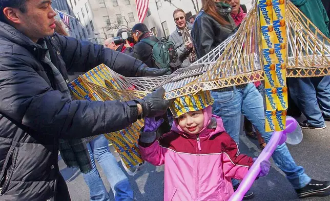 FILE - Russell Chin, left, helps Angie Hoyle, 3, of the Brooklyn borough of New York, as she tries on a hat made of MetroCards shaped as the Brooklyn Bridge during the Easter Parade on New York's Fifth Avenue, March 23, 2008. (AP Photo/Tina Fineberg, File)
