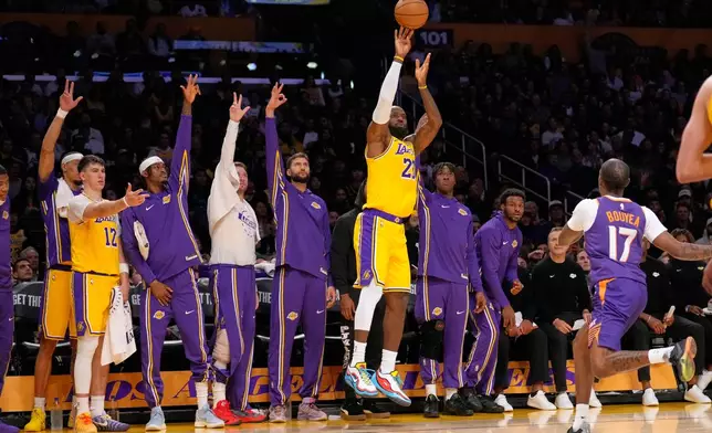 Los Angeles Lakers forward LeBron James, center, shoots as his teammates gesture from the bench while Phoenix Suns guard Jamaree Bouyea, right, defends during the first half of an NBA basketball game Monday, Dec. 1, 2025, in Los Angeles. (AP Photo/Mark J. Terrill)