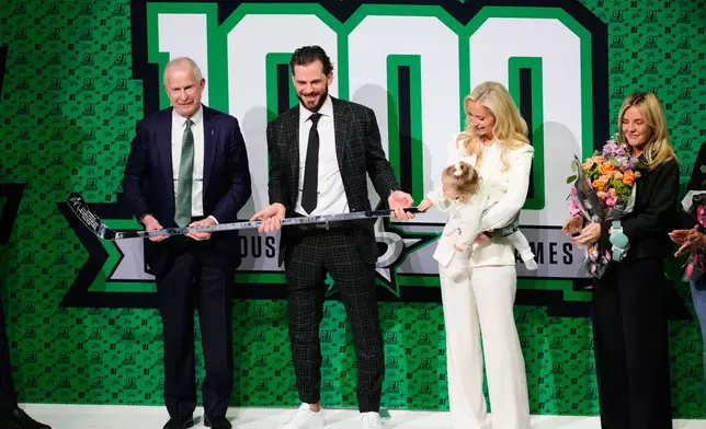Dallas Stars General Manager is Jim Nill, left, presents Tyler Seguin, center, with a 1000-game trophy stick as he wife Kate, and child look on before an NHL hockey game agianst the Florida Panthers in Dallas, Saturday, Dec. 13, 2025. (AP Photo/Tony Gutierrez)