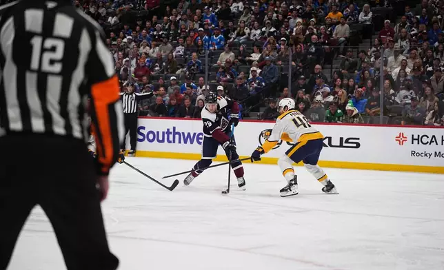 Colorado Avalanche center Nathan MacKinnon, left, shoots the puck past Nashville Predators defenseman Nick Perbix for a goal in the first period of an NHL hockey game, Saturday, Dec. 13, 2025, in Denver. (AP Photo/David Zalubowski)