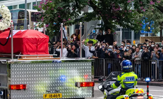 People gather outside a funeral parlor to pay tribute to Ho Wai-ho, the firefighter who lost his life in the line of duty during the deadly fire at Wang Fuk Court on Nov. 26, passing by a funeral parlor in Hong Kong, Friday, Dec. 19, 2025. (AP Photo/Chan Long Hei)