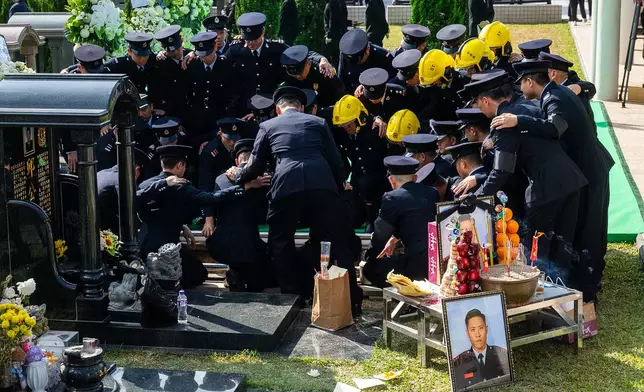 Firefighters gather around the grave of Ho Wai-ho, the firefighter who lost his life in the line of duty during the deadly fire at Wang Fuk Court on Nov. 26, during a funeral in Hong Kong, Friday, Dec. 19, 2025. (AP Photo/Chan Long Hei)