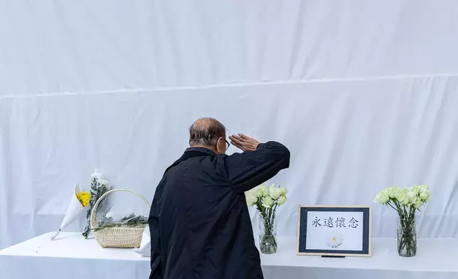 A resident salutes to pay tribute to Ho Wai-ho, the firefighter who lost his life in the line of duty during the deadly fire at Wang Fuk Court on Nov. 26, in Hong Kong, Friday, Dec. 19, 2025. (AP Photo/Chan Long Hei)