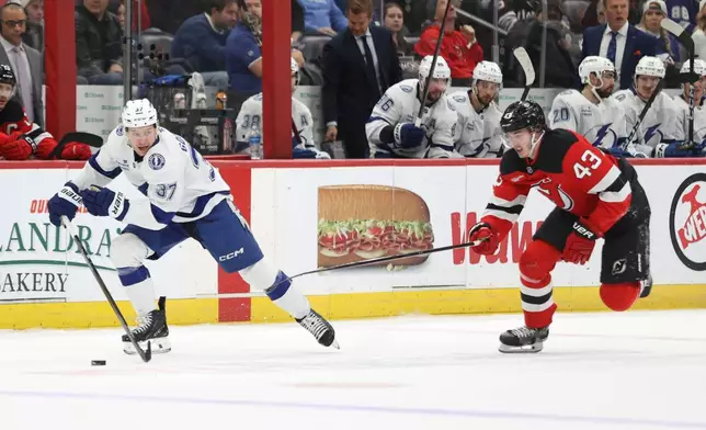 New Jersey Devils' Luke Hughes (43) attempts to steal the puck from Tampa Bay Lightning's Yanni Gourde (37) during the first period of an NHL hockey game Thursday, Dec. 11, 2025, in Newark, N.J. (AP Photo/Pamela Smith)