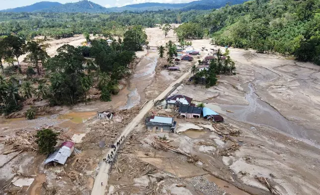 FILE - People walk along a road in a village affected by a flash flood in Batang Toru, North Sumatra, Indonesia, Dec. 1, 2025. (AP Photo/Binsar Bakkara, File)