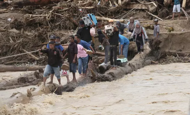 FILE - Flood survivors use logs to cross a river in Batang Toru, North Sumatra, Indonesia, Dec. 2, 2025. (AP Photo/Binsar Bakkara, File)