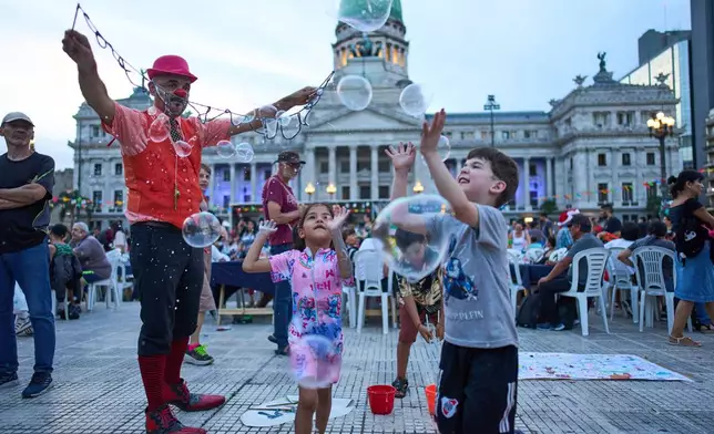 Children play with bubbles during a Christmas dinner organized by labor activists for people in need outside Congress in Buenos Aires, Argentina, Wednesday, Dec. 24, 2025. (AP Photo/Rodrigo Abd)