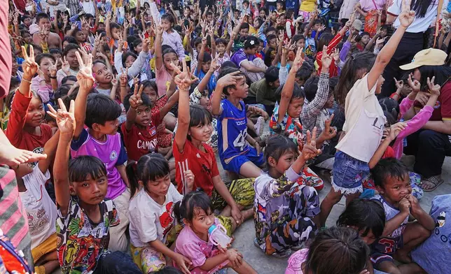 Children raise their hands while receiving donation from charity as they take refuge in Banteay Menchey provincial town, Cambodia, Saturday, Dec. 13, 2025, after fleeing homes following fighting between Thailand and Cambodia. (AP Photo/Heng Sinith)