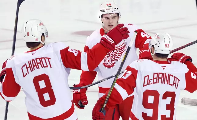 Detroit Red Wings' Axel Sandin-Pellikka (44) celebrates with Alex DeBrincat (93) and Ben Chariot (8) after scoring against the Calgary Flames during the first period of an NHL hockey game in Calgary, Alberta, on Wednesday, Dec. 10, 2025. (Larry MacDougal/The Canadian Press via AP)