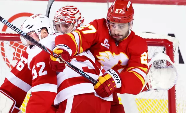 Detroit Red Wings' Travis Hamonic (52) battles with Calgary Flames' Matt Coronato (27) in front of Red Wings goalie John Gibson during the second period of an NHL hockey game in Calgary, Alberta, on Wednesday, Dec. 10, 2025. (Larry MacDougal/The Canadian Press via AP)