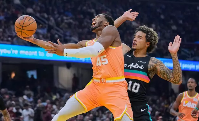 Cleveland Cavaliers guard Donovan Mitchell (45) drives to the basket past San Antonio Spurs forward Jeremy Sochan (10) in the first half of an NBA basketball game Friday, Dec. 5, 2025, in Cleveland. (AP Photo/Sue Ogrocki)