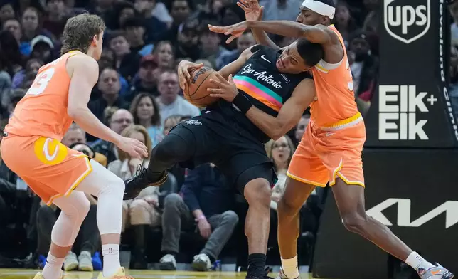 San Antonio Spurs forward Keldon Johnson, center, loses control of the ball between Cleveland Cavaliers forward Luke Travers, left, and forward Nae'Qwan Tomlin, right, in the first half of an NBA basketball game Friday, Dec. 5, 2025, in Cleveland. (AP Photo/Sue Ogrocki)