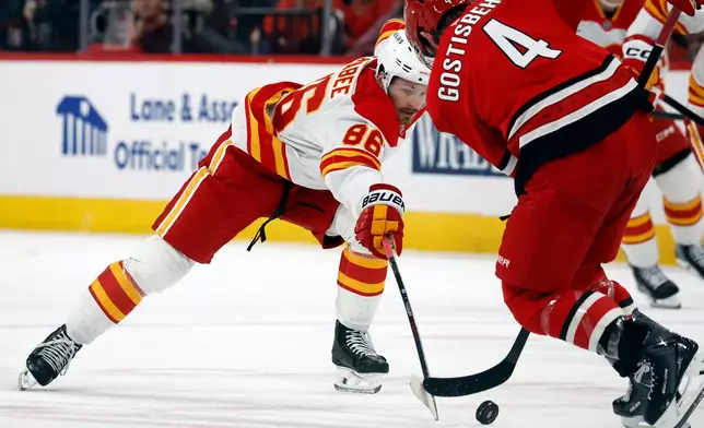 Calgary Flames' Joel Farabee (86) stretches for the puck as he approaches Carolina Hurricanes' Shayne Gostisbehere (4) during the first period of an NHL hockey game in Raleigh, N.C., Sunday, Nov. 30, 2025. (AP Photo/Karl DeBlaker)