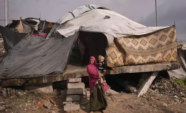 A woman holds a child as they stand in front of their tent in a makeshift camp for displaced Palestinians set up in an area in Gaza City, Monday, Dec. 29, 2025. (AP Photo/Jehad Alshrafi)